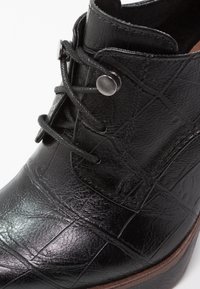 Botte en cuir noir avec une surface texturée, œillets métalliques ronds et lacets noirs sur une semelle marron, vue en gros plan.