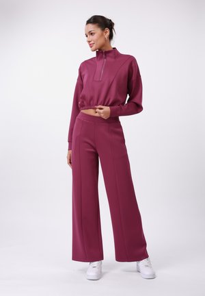 Fitted maroon cropped athletic top with high collar and zip, paired with wide-leg matching pants, both in smooth fabric, worn with white sneakers.