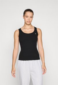 Musträbade musta tank top ümarate kaelustega ja kitsas sobivus, millel on väike logo aktsent. Kombineeritud heledate hallide dressipükstega.