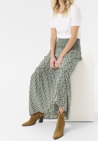 Maxi nederdel med grønt blomsterprint, let stof, elastisk talje, parret med lysebrune ruskinds ankelstøvler og en hvid ribbet top.