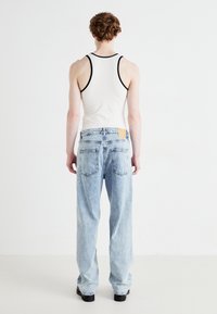 Jeans de color azul claro con un ajuste holgado, textura desgastada, dos bolsillos traseros, parche de cuero en la cinturilla y una camiseta sin mangas blanca con ribetes negros.