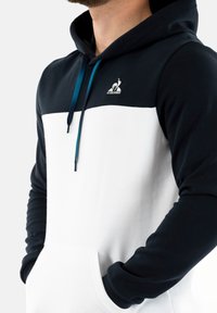 Felpa con cappuccio caratterizzata da una parte superiore blu navy e una sezione inferiore bianca, in tessuto morbido, con tasca a canguro e coulisse a contrasto.