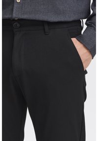 Czarne spodnie o gładkiej fakturze, z zapięciem na guzik i bocznymi kieszeniami. Połączone z ciemnoszarym shirtem, prezentującym smukły krój.
