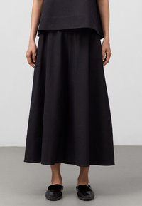 Svart, texturerad knä-lång kjol med en bred, flödande design. Kombinerad med enkla svarta slip-on skor. Modern, minimalistisk estetik.