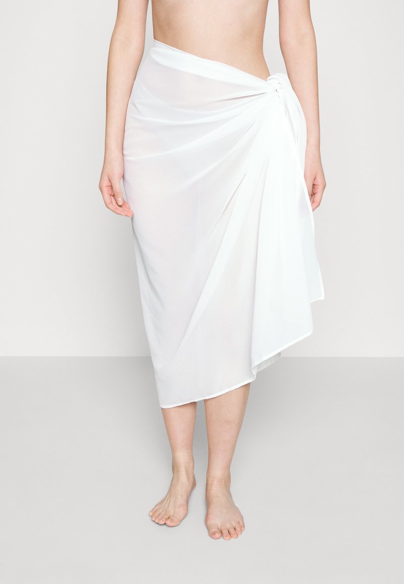 Falda blanca y transparente hecha de tela ligera, con un diseño drapeado y un detalle anudado en la cintura.