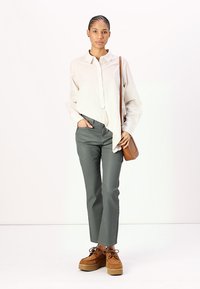 Lys beige, langermet skjorte med krage; olivengrønne, rette bukser; sandfarvede platåsko; liten brun crossbody-veske.