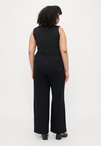 Combinaison noire sans manches avec une taille élastique, un design à jambes larges, deux poches au dos et une texture de tissu lisse.