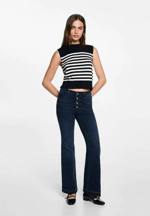 Mustavalkoraidallinen hihaton crop-top, joka on yhdistetty tummansiniset leveälahkeisiin farkkuihin, joissa on nappi etuosassa ja repaleinen helma. Mustat kengät täydentävät asun.