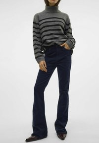 Pull à col roulé gris rayé avec des rayures foncées, associé à un pantalon en velours côtelé bleu marine évasé. Le pull a des manches longues ; le pantalon a une coupe classique.