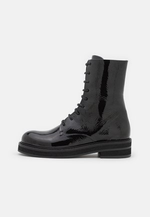 Schwarzer Schnürstiefel aus Lackleder mit dicker Sohle und niedrigem Blockabsatz, seitlich auf weißem Hintergrund dargestellt.