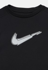Črn majica s krožnim ovratnikom z izkrivljenim belim in sivo Nike swoosh logotipom, ki je postavljen na sredini prsnega dela.