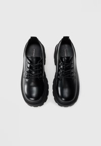 Black leather lace-up shoes with a smooth finish, rounded toe, and ribbed rubber sole. Features six eyelets and a pull tab on the heel.