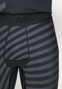 Mallas deportivas de rayas negras con un diseño ajustado, que cuentan con una cinturilla ancha grabada con "ADIDAS". Textura suave y material elástico.
