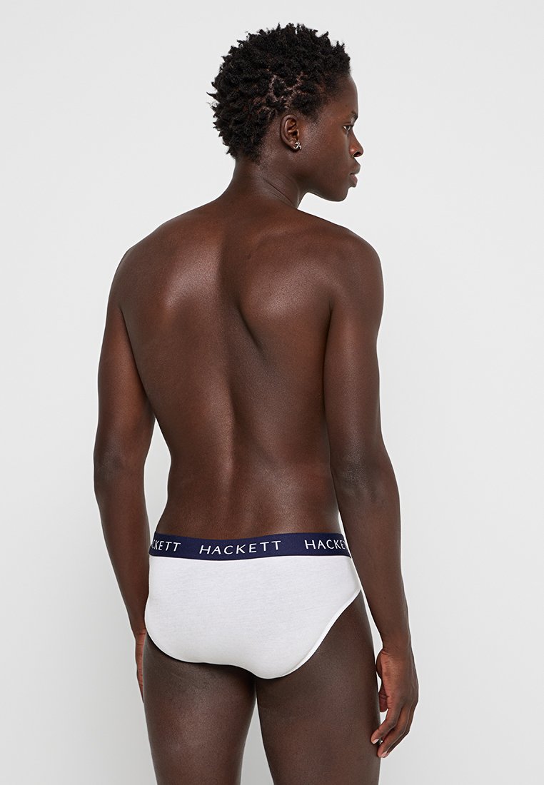 Bañador blanco para hombre con cinturilla elástica azul marino que presenta la marca "HACKETT". Material de algodón suave, ajuste ceñido y diseño minimalista.