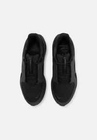 Chaussures de sport noires avec une texture matelassée, un bout arrondi et une semelle rembourrée. Équipées de lacets noirs et d'un logo discret sur le côté.