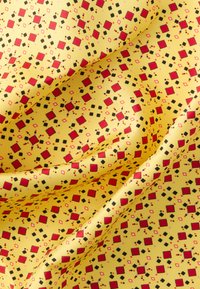 Tela amarilla texturizada con un patrón geométrico repetitivo de cuadros rojos, diamantes negros y pequeños detalles rosas.