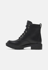 Bottines en cuir noir avec un bout rond, œillets en métal, lacets à l'avant, tirant au dos et tissu texturé sur le col. Talon bas.