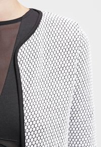 Biało-czarny teksturowany kardigan z wzorem plastra miodu, ozdobiony zakrzywioną czarną lamówką i warstwową konstrukcją z tkaniny pod spodem.