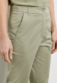 Light green trousers with a smooth texture, featuring a button closure, side pockets, and front pleats for added detail.