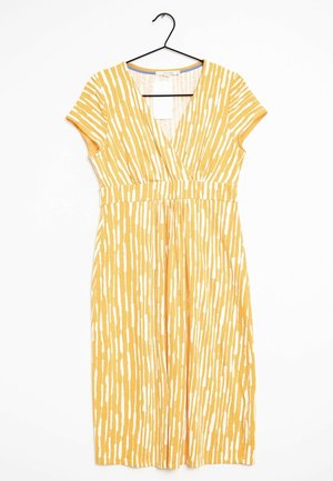 Robe jaune avec un motif de rayures verticales blanches, manches courtes, décolleté en V et taille cintrée, suspendue sur un cintre noir contre un fond blanc.