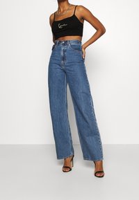 Svart kortärmad croptop med gröna broderade detaljer, kombinerad med högmidjade, vida jeans i ljusblå denim. Accessoarerna inkluderar svarta högklackade skor.