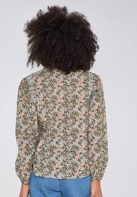 Långärmad blus i ljusblått tyg med grön och rosa blommönster, med puffärmar och rundad nederkant.