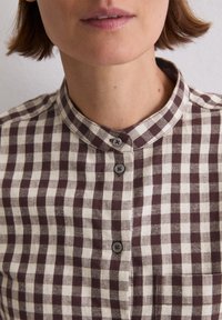 Brown and cream checked shirt with a mandarin collar, featuring buttons and a chest pocket, made of a textured fabric.