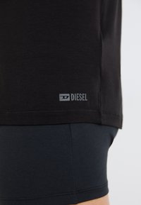 T-shirt noir en tissu doux, affichant un petit logo gris "DIESEL" près de l'ourlet, associé à un short bleu foncé.