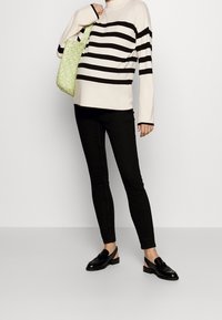 Svetr s černobílými pruhy, černé slim kalhoty, černé nazouvací boty a zelená pletená taška. Hladké textury a jednoduchý design.