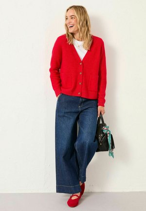 Red cardigan made of soft fabric, featuring two front pockets and button closure, paired with wide-leg denim jeans and red shoes.