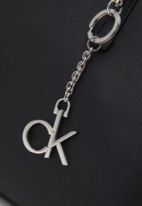 Sort tekstureret håndtaske med en sølv kæde og hardware. Har et fremtrædende sølv "ck" logo charme vedhæftet.