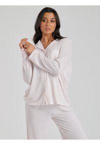 Completo pigiama rosa chiaro con righe verticali, composto da una camicia con bottoni e maniche lunghe, abbinato a pantaloni coordinati. Tessuto morbido e strutturato.