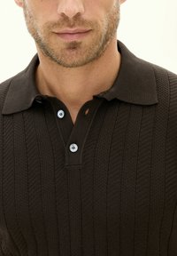 Mörkbrun stickad pikétröja med ribbad textur, en vikt krage och tre knappar med ljusblå detaljer.