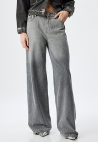 Jeans de mezclilla gris de pierna ancha con un acabado desgastado, que presentan un diseño de cinco bolsillos y pasadores para cinturón. La tela tiene un aspecto texturizado.