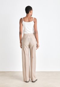 Pantaloni beige a gamba larga con un tessuto testurizzato, abbinati a una maglietta bianca senza maniche con spalline sottili, mostrati da dietro su uno sfondo chiaro.
