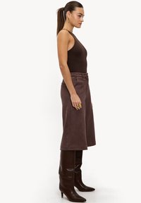Justaucorps marron associé à un pantalon marron en suédine synthétique, taille haute et jambes larges, ainsi qu'à des bottes en cuir marron montant jusqu'aux genoux, à bout pointu.