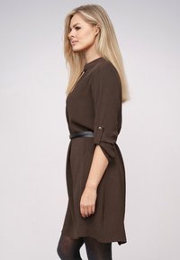 Braunes, strukturiertes Kleid mit einem geknöpften Hochrollärmel und einem schwarzen Gürtel in der Taille. Einfaches Design mit einem runden Ausschnitt und einer legeren Passform.