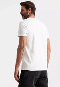 Camiseta blanca de manga corta con cuello redondo, hecha de algodón. Vista desde la parte posterior, presenta una textura suave y un ajuste casual.