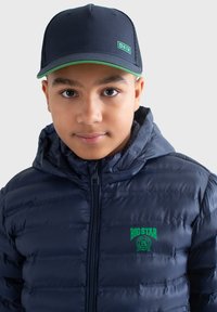 Námo�řnická puffer bunda se zipovým uzávěrem, se dvěma horizontálními prošívanými detaily a zeleným logem. Černá čepice se zelenými akcenty a síťovanými částmi.