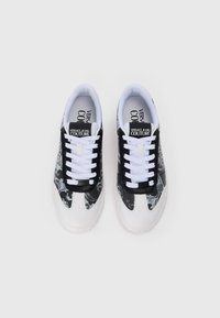 Črne in bele teniske z cvetličnim vzorcem, belimi vezalkami in teksturiranim podplatom. Imajo blagovno znamko na ježku in stranskih panelih.