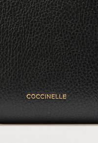 Musta nahkainen lompakko, jossa on teksturoitu pinta ja etupuolella kohokuvioitu kullanvärinen "COCCINELLE"-logo. Yksinkertainen, suorakaiteenmuotoinen muotoilu.