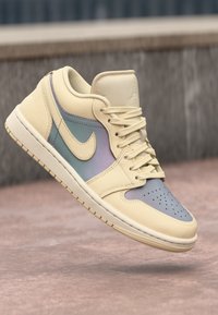 Krém színű sneaker pasztell akcentusokkal, elmosódott háttér előtt kiemelve, klasszikus formatervezéssel és részletes varrással.
