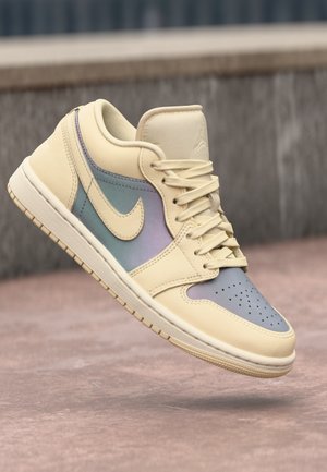 Cream-colored sneaker with pastel accents, highlighted against a blurred background, showcasing classic design and detailed stitching.