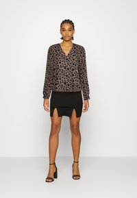 Blusa de mangas longas e decote em V em tecido castanho com padrão floral preto; combinada com uma saia preta justa com uma fenda frontal.