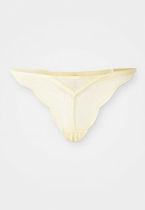 Lichtgele kant thong onderbroek met golvende randen en een delicaat bloemenpatroon, plat weergegeven op een witte achtergrond.