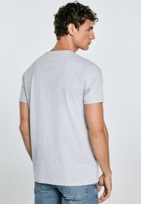 Pilkas trumpų rankovių marškinėlis, pagamintas iš minkštos medvilnės mišinio, su apvalia iškirpte ir laisvu siluetu, pasižymintis lygiu paviršiumi ir minimalistiniu dizainu.