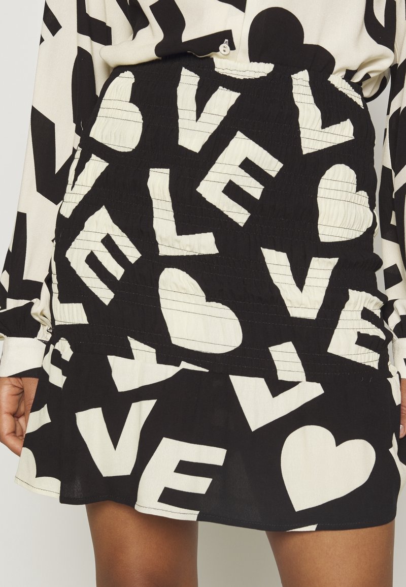 Gonna e blusa in bianco e nero con lettere "LOVE" audaci e un motivo a forma di cuore, parzialmente visibili sul torace inferiore e sulla mano di una persona.