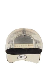 Adjustable cap with a structured front in cream fabric, mesh backing, and a black visor. Features a branded label at the underside.
