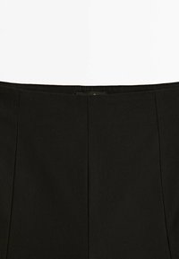 Gros plan sur la ceinture d'une jupe noire avec des détails de coutures verticales et une petite étiquette en tissu au centre du dos.