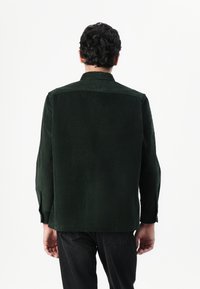 Dark green corduroy shirt, featuring a button-down collar, long sleeves, and vertical ribbing texture. Back view shows a straight cut.
